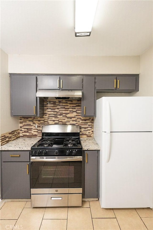 kitchen featuring under cabinet range hood, gray cabinetry, backsplash, freestanding refrigerator, and gas range