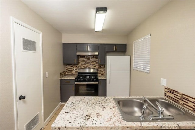 kitchen with tasteful backsplash, freestanding refrigerator, stainless steel gas stove, a sink, and under cabinet range hood