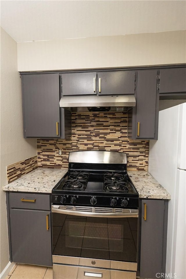 kitchen featuring stainless steel gas stove, gray cabinetry, freestanding refrigerator, and decorative backsplash