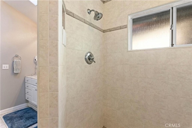 bathroom featuring a tile shower, vanity, and baseboards