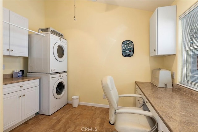 laundry room with stacked washer / drying machine, cabinet space, and baseboards