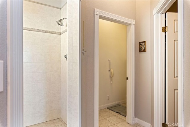 bathroom with a tile shower, baseboards, and tile patterned floors