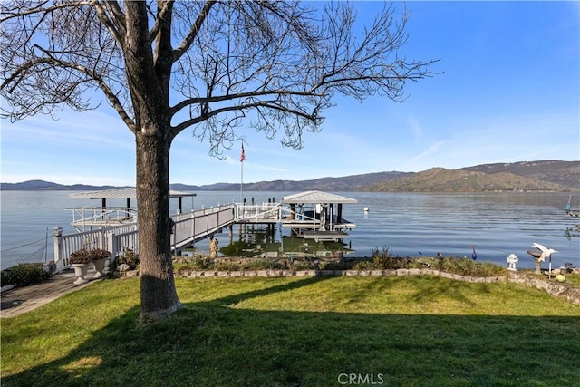 view of dock featuring a water and mountain view, boat lift, and a lawn