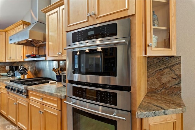 kitchen featuring wall chimney exhaust hood, appliances with stainless steel finishes, light brown cabinetry, and tasteful backsplash