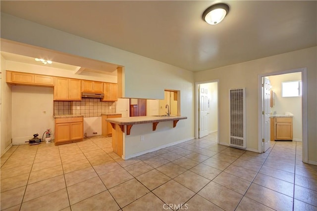 kitchen with decorative backsplash, a breakfast bar area, under cabinet range hood, a sink, and light tile patterned flooring