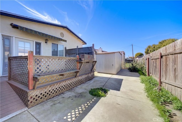 view of patio featuring an outbuilding, a storage unit, a fenced backyard, driveway, and a wooden deck