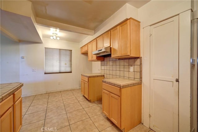 kitchen featuring tasteful backsplash, under cabinet range hood, tile countertops, and light tile patterned floors