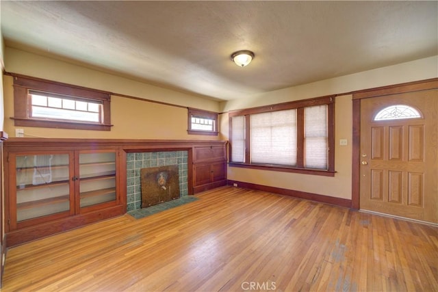 unfurnished living room featuring a tile fireplace, light wood-style flooring, and baseboards