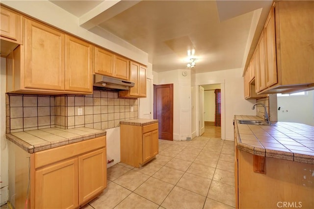 kitchen with light tile patterned floors, tile counters, decorative backsplash, a sink, and under cabinet range hood