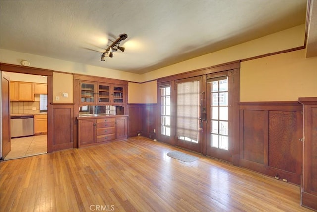 interior space with dishwasher, a wainscoted wall, light wood-style flooring, glass insert cabinets, and french doors