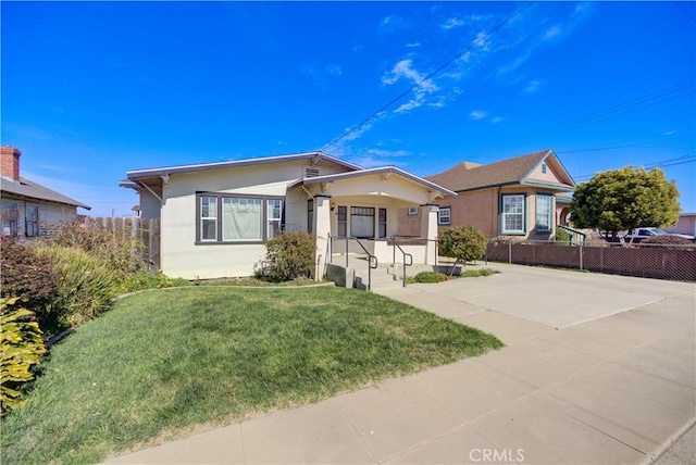 bungalow-style home with a front yard, fence, and stucco siding