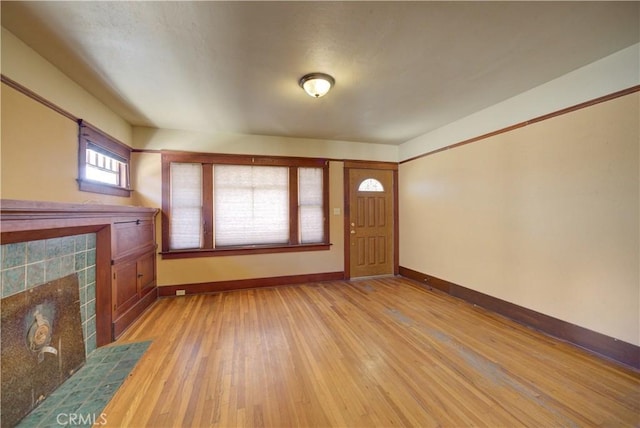 foyer featuring light wood finished floors, a tile fireplace, and baseboards