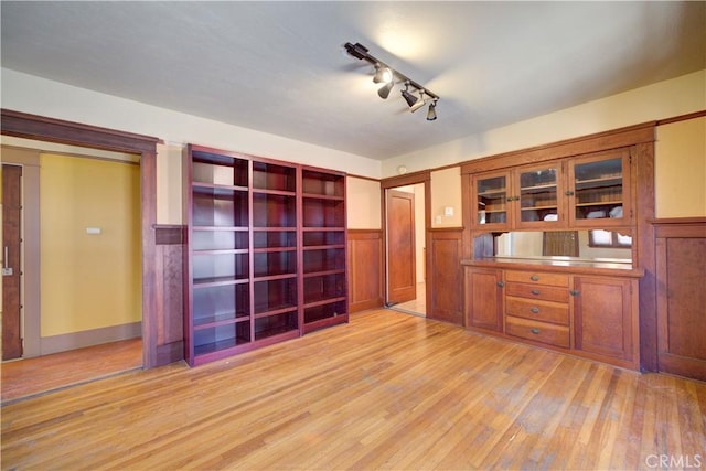 unfurnished office featuring light wood-type flooring, a wainscoted wall, and track lighting