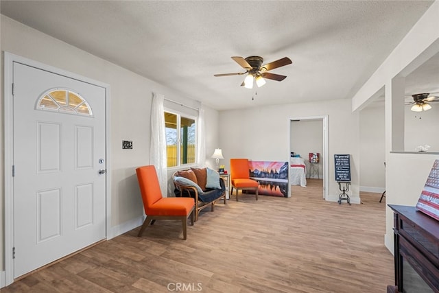 living area with baseboards, a textured ceiling, a ceiling fan, and wood finished floors