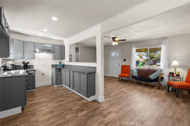 kitchen with under cabinet range hood, open floor plan, a sink, and gray cabinetry