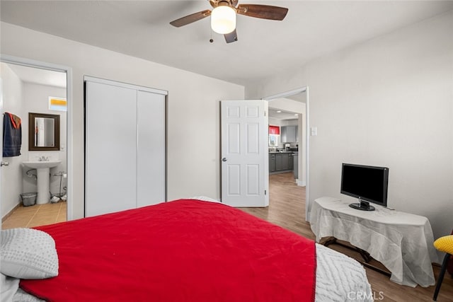 bedroom featuring wood finished floors, a sink, a ceiling fan, a closet, and ensuite bath