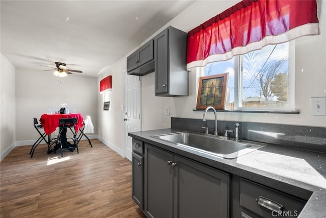 kitchen with wood finished floors, a sink, a ceiling fan, and baseboards