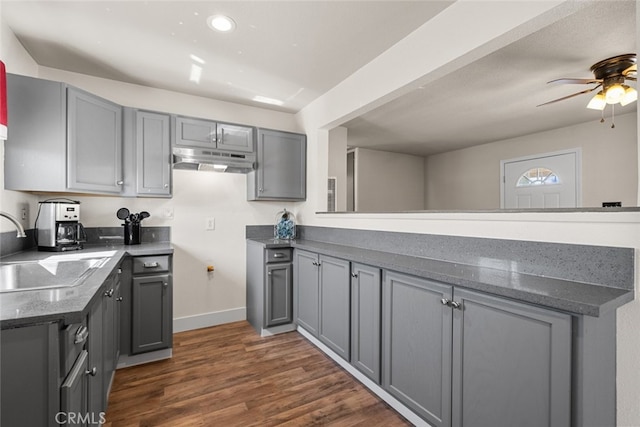 kitchen featuring gray cabinets, dark wood-type flooring, a sink, a peninsula, and under cabinet range hood