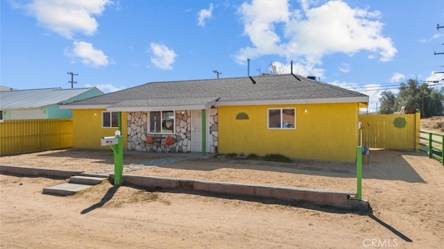 back of house featuring stone siding, fence, and stucco siding