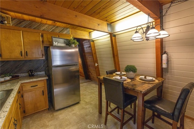 kitchen featuring beam ceiling, brown cabinetry, freestanding refrigerator, and wooden walls