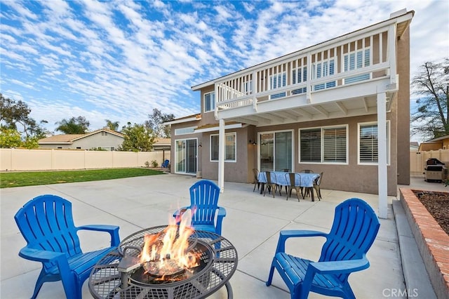 rear view of house featuring an outdoor fire pit, fence, a balcony, and stucco siding