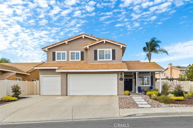 traditional-style home featuring an attached garage, fence, concrete driveway, and stucco siding