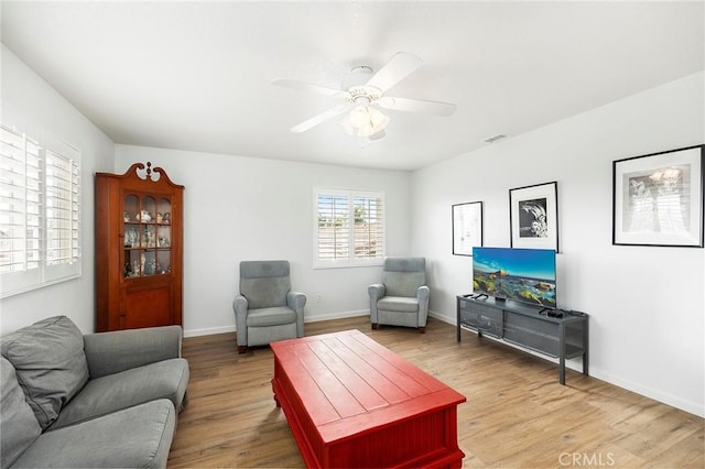 living room with a ceiling fan, visible vents, light wood-style flooring, and baseboards