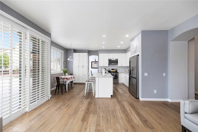 kitchen featuring arched walkways, light wood-style flooring, a kitchen breakfast bar, open floor plan, and appliances with stainless steel finishes