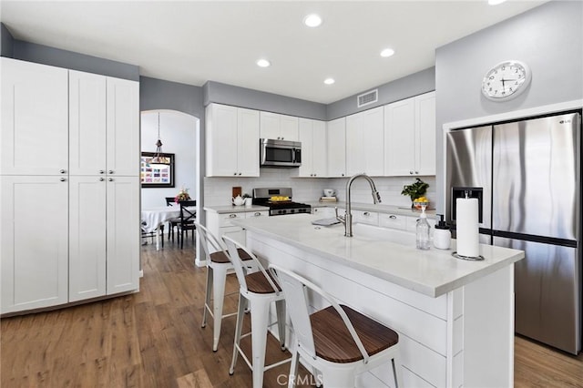 kitchen with tasteful backsplash, white cabinets, a kitchen breakfast bar, wood finished floors, and stainless steel appliances