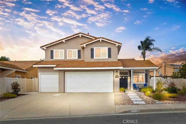 traditional-style house with fence, driveway, an attached garage, and stucco siding