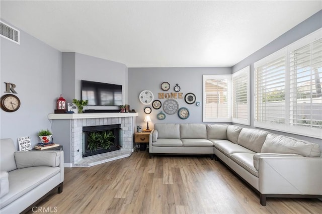 living area with a brick fireplace, wood finished floors, and visible vents