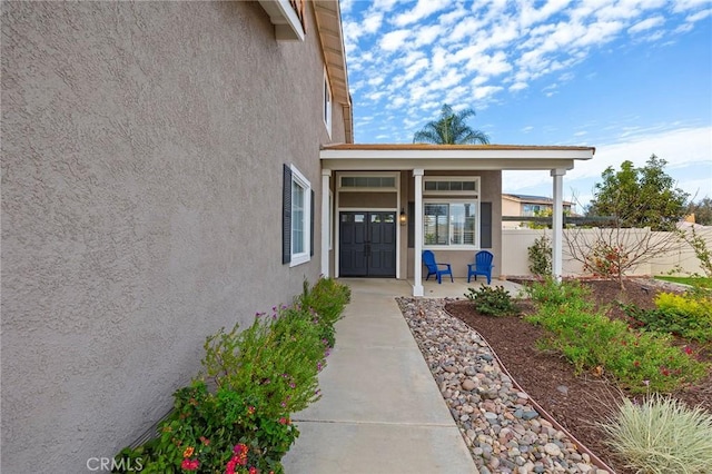 view of exterior entry with covered porch, fence, and stucco siding