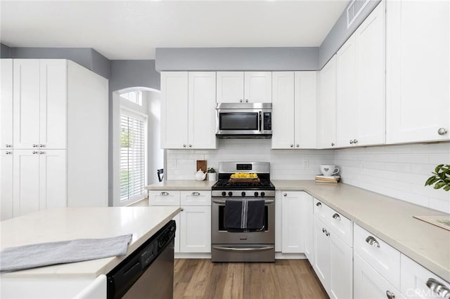 kitchen with stainless steel appliances, wood finished floors, white cabinets, light countertops, and tasteful backsplash