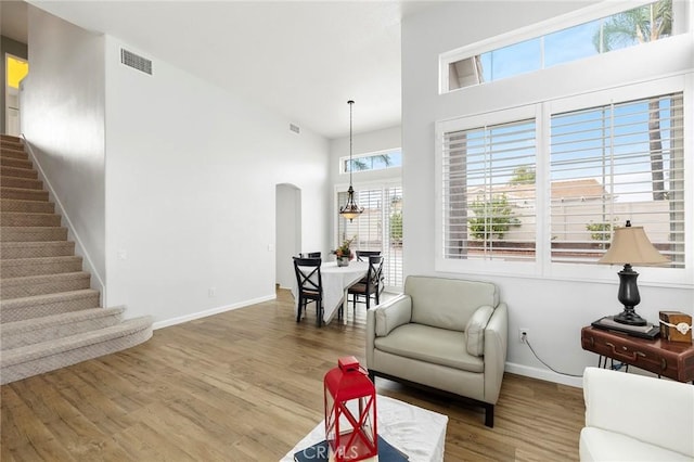 sitting room with arched walkways, visible vents, a high ceiling, wood finished floors, and stairs