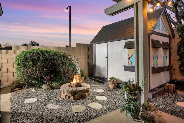 outdoor structure at dusk featuring an outdoor fire pit, a fenced backyard, an outdoor structure, and a storage unit