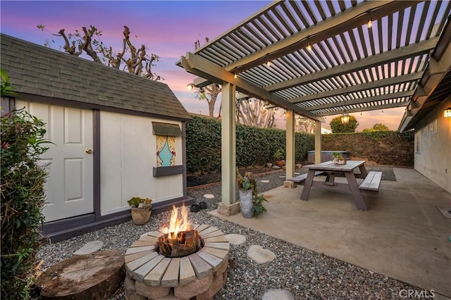 patio terrace at dusk featuring an outbuilding, outdoor dining area, a fenced backyard, a fire pit, and a pergola