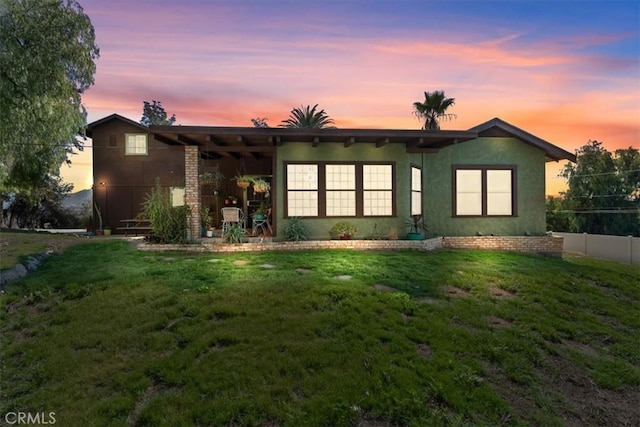 rear view of property with a yard, fence, and stucco siding