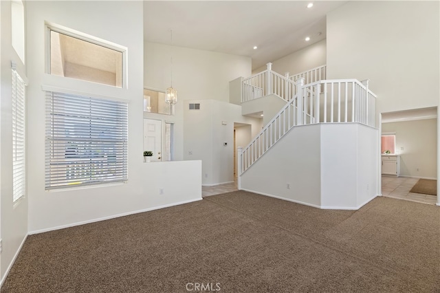 unfurnished living room featuring a towering ceiling, visible vents, stairs, baseboards, and carpet