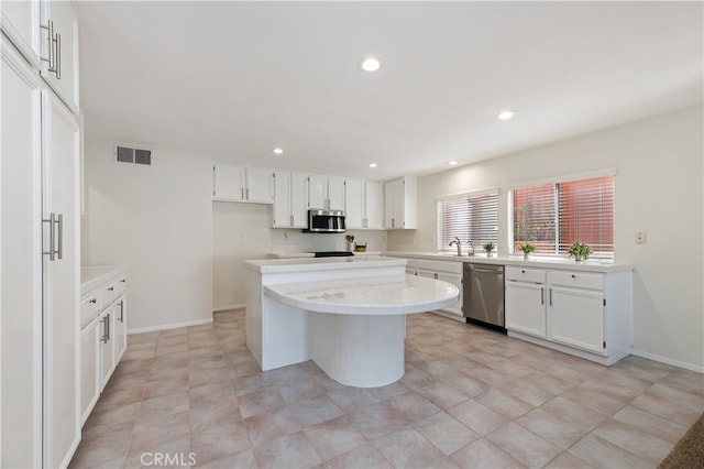 kitchen featuring visible vents, a kitchen island, stainless steel appliances, light countertops, and white cabinetry