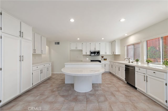 kitchen featuring stainless steel appliances, a sink, visible vents, white cabinets, and a center island