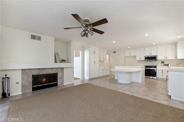 kitchen featuring stainless steel appliances, visible vents, a tiled fireplace, white cabinetry, and a kitchen island