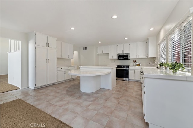 kitchen with stainless steel appliances, a kitchen island, tile counters, and white cabinetry