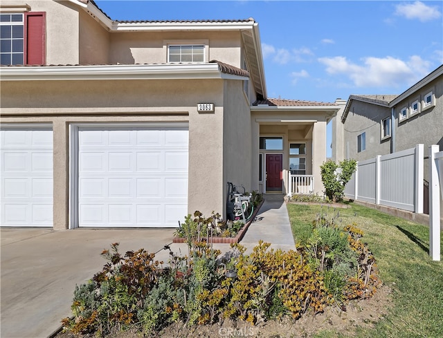 view of front of property featuring a garage, concrete driveway, a tile roof, fence, and stucco siding