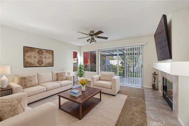 living area with light tile patterned floors, ceiling fan, a tile fireplace, and baseboards