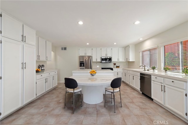 kitchen featuring white cabinets, appliances with stainless steel finishes, a center island, a kitchen bar, and a sink