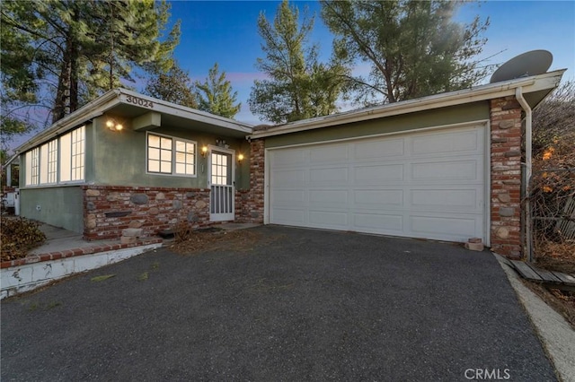 view of front of property with a garage, stone siding, driveway, and stucco siding