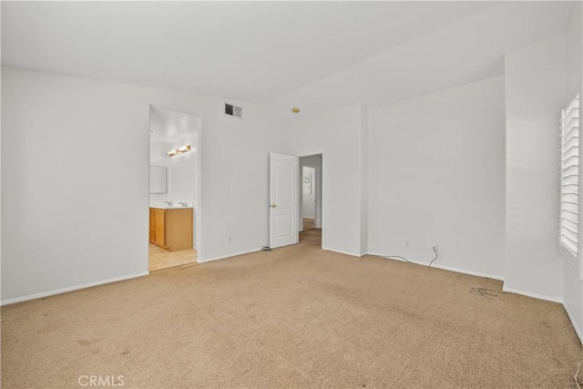 unfurnished bedroom with baseboards, ensuite bath, visible vents, and light colored carpet