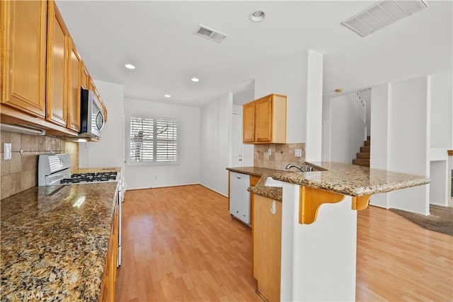 kitchen featuring a peninsula, white appliances, light wood-type flooring, and visible vents