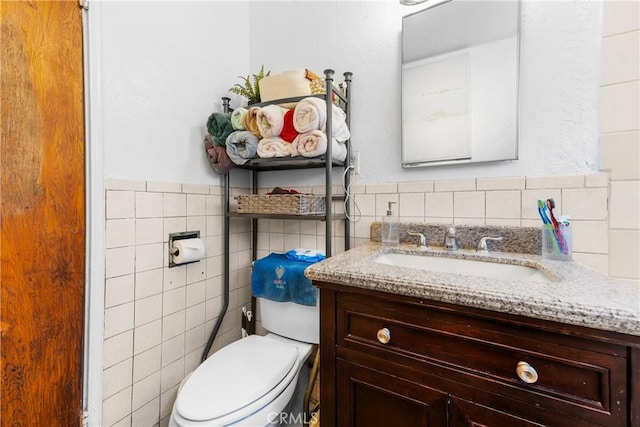 half bath with a wainscoted wall, vanity, toilet, and tile walls