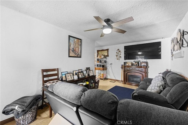 living room with ceiling fan, a textured ceiling, a fireplace, and tile patterned flooring